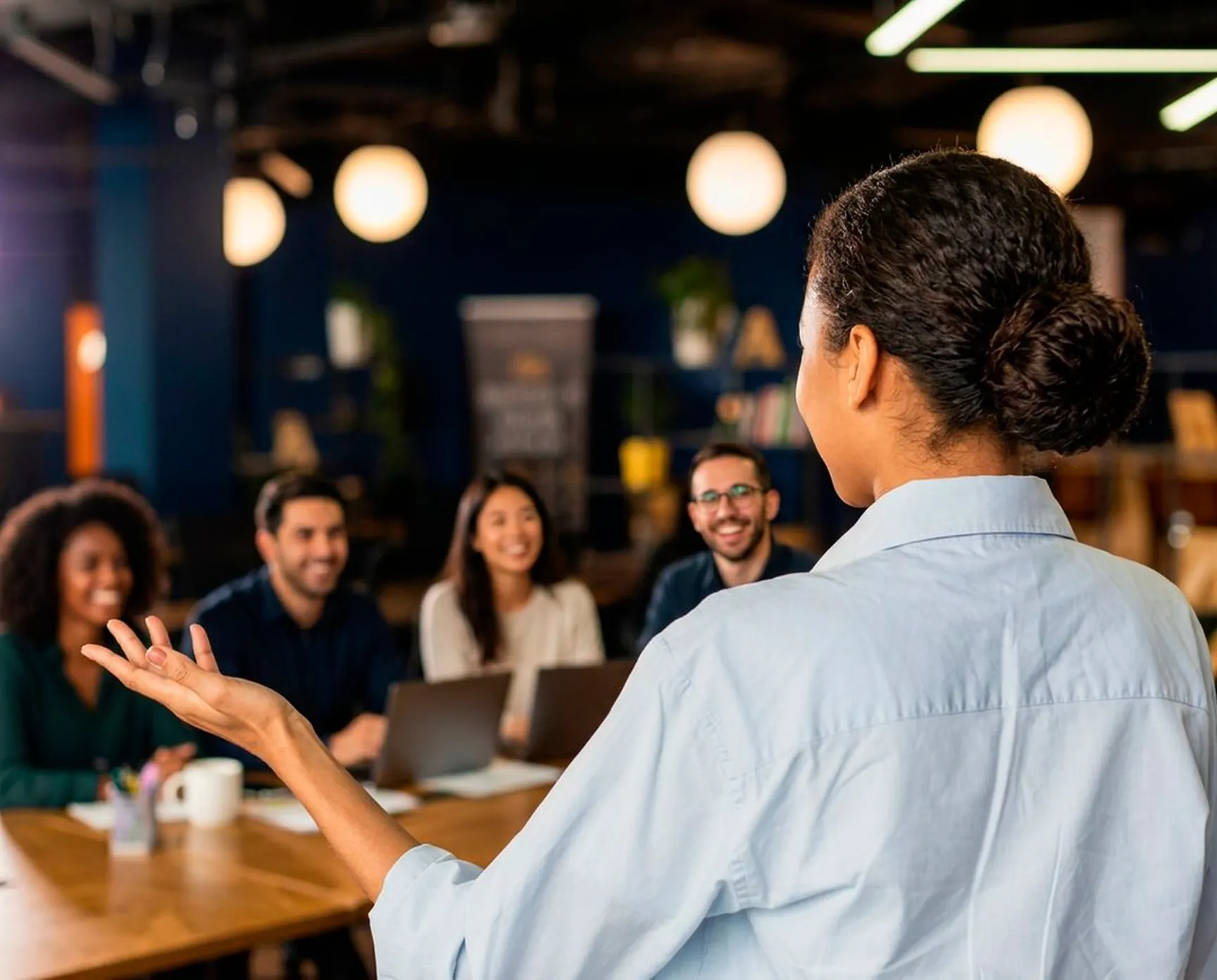 Consultora conduzindo uma palestra para um grupo de colaboradores reunidos em volta da mesa.